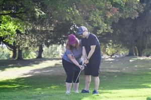 Person with visual impairment playing golf with the help pf a guide